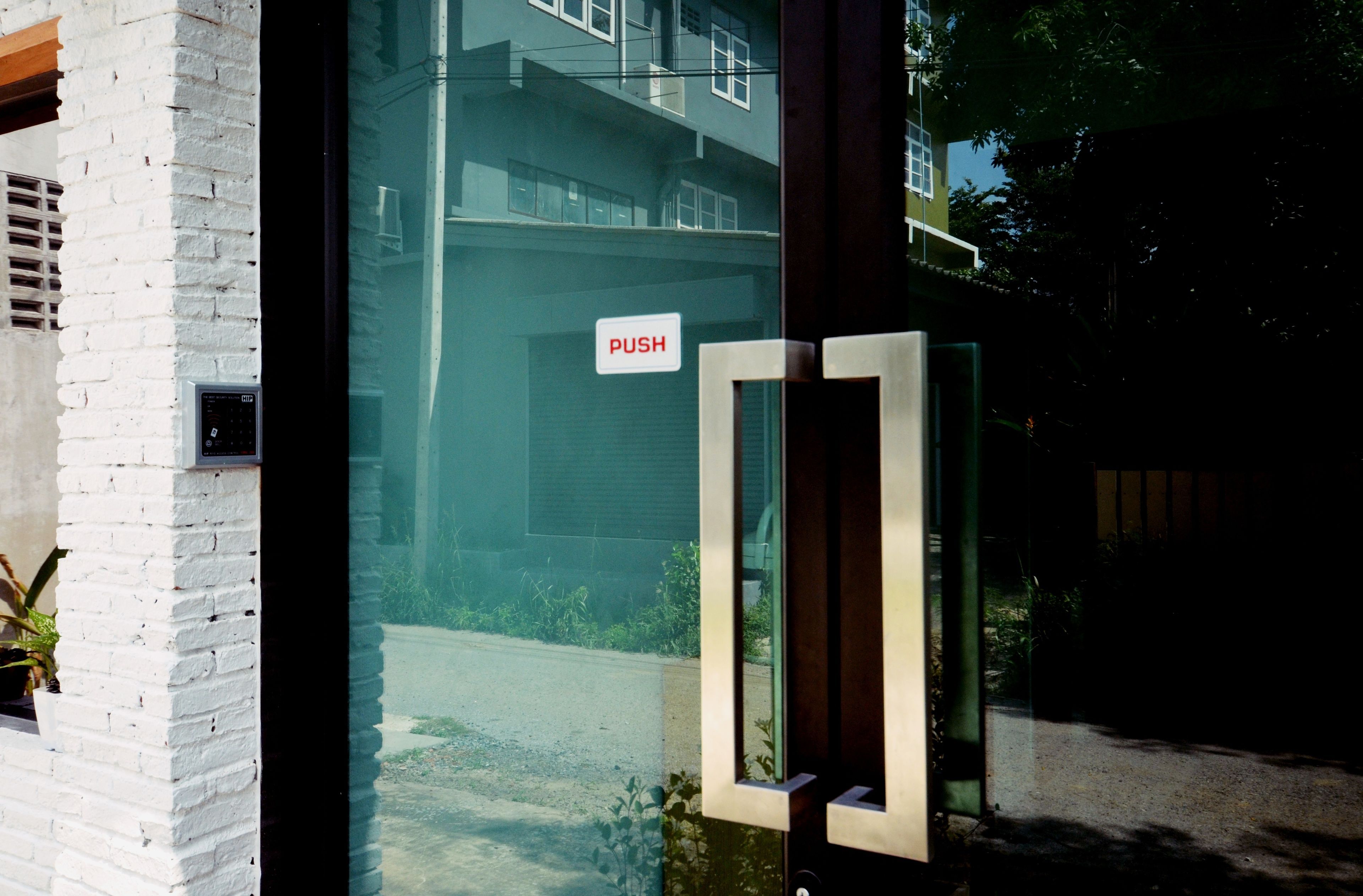 A glass door with a 'PUSH' sign, a keypad, and a view of a building with balconies.