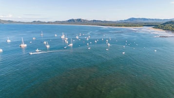 Vista aérea de una zona costera con numerosos barcos anclados en el agua, rodeada por un paisaje montañoso.