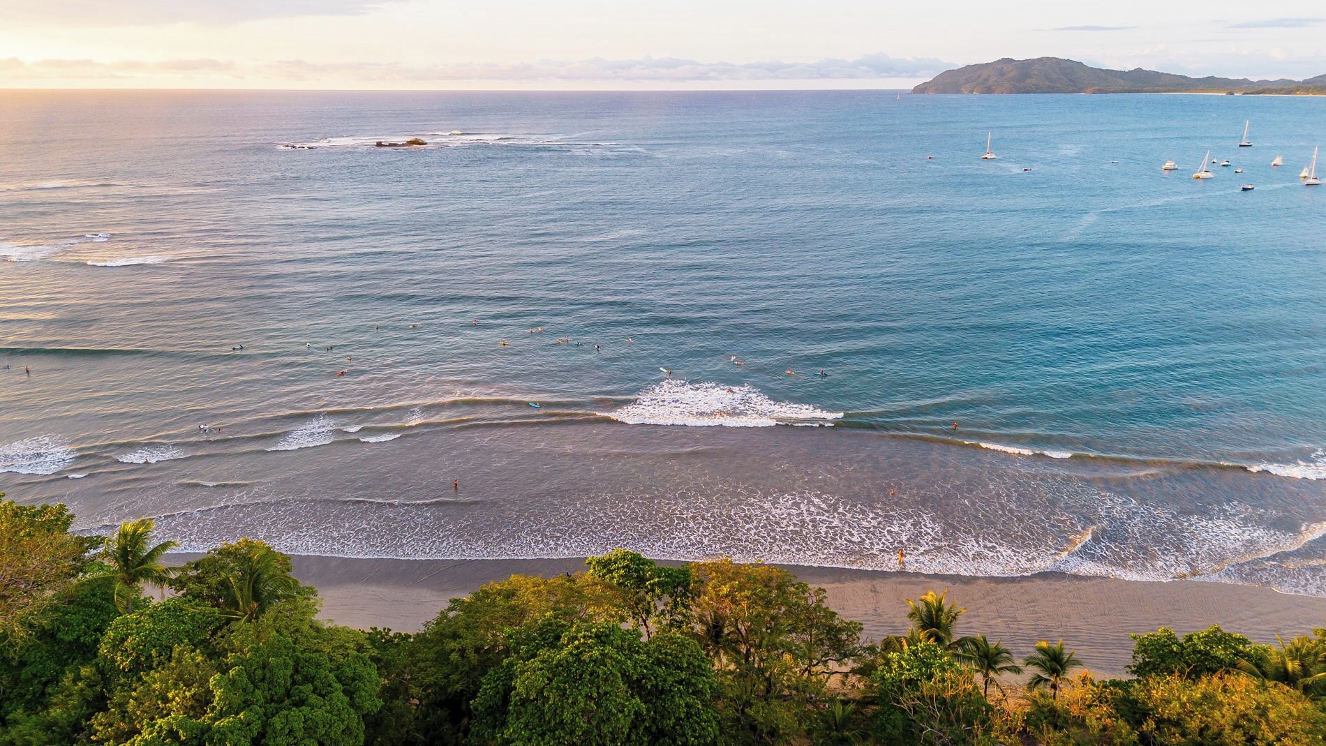 Ein Strand mit Wellen, Booten und einer entfernten Insel.