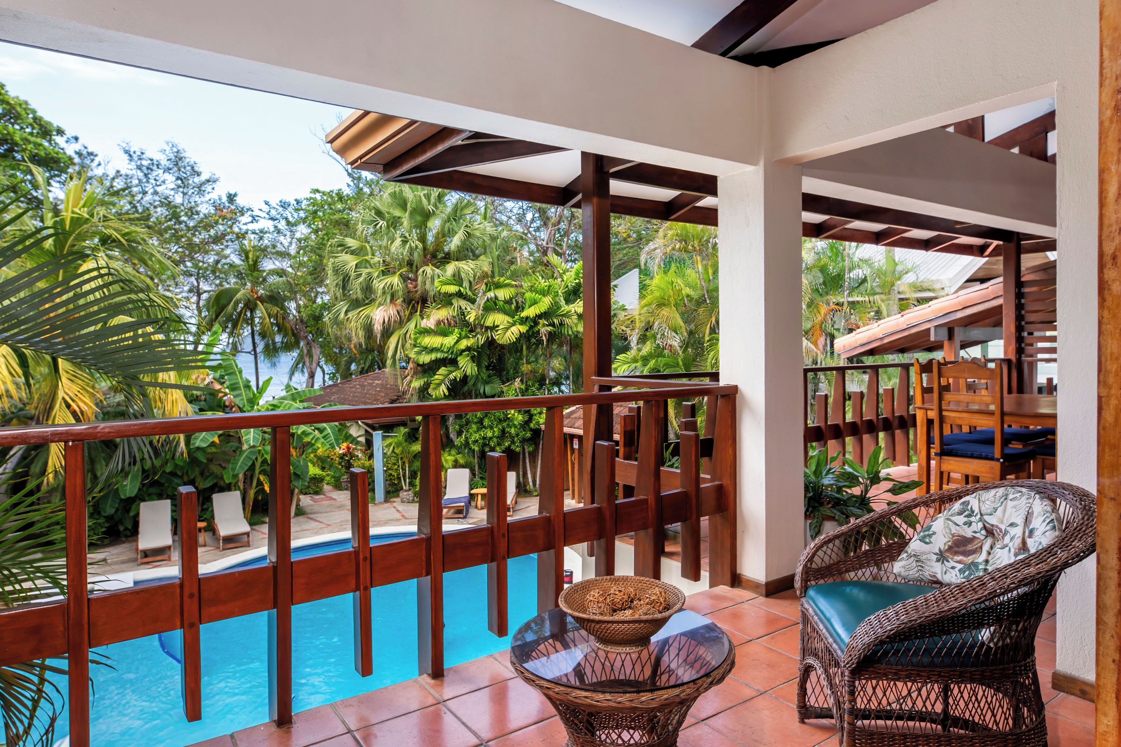 A balcony with a pool, wicker furniture, and a view of palm trees.