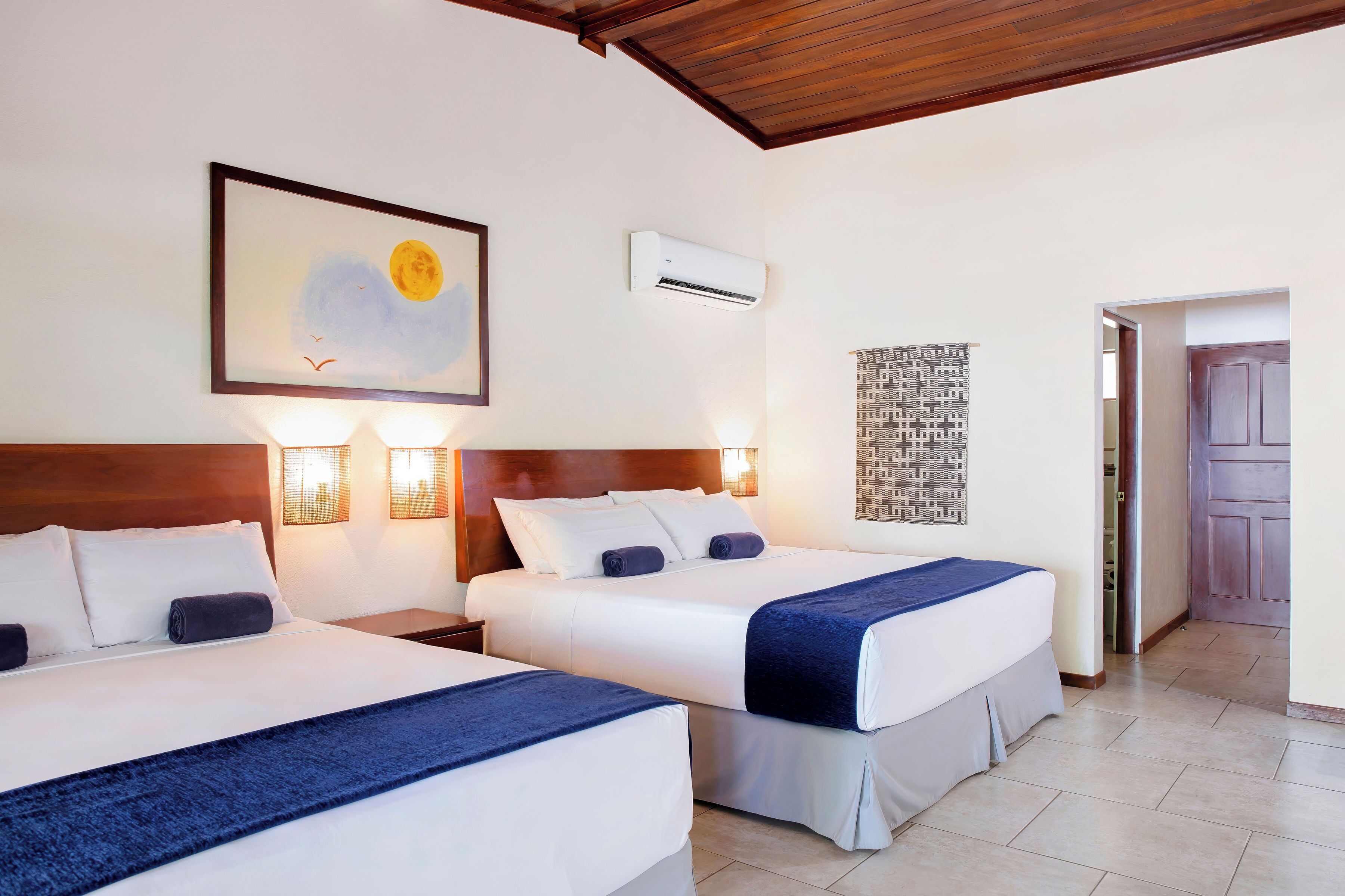 Une chambre d’hôtel avec deux lits, un ventilateur de plafond, un appareil de climatisation et un tableau au mur.