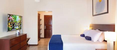 Une chambre d’hôtel avec un lit, un téléviseur posé sur une commode en bois, un tableau accroché au mur et une porte donnant sur une autre pièce.