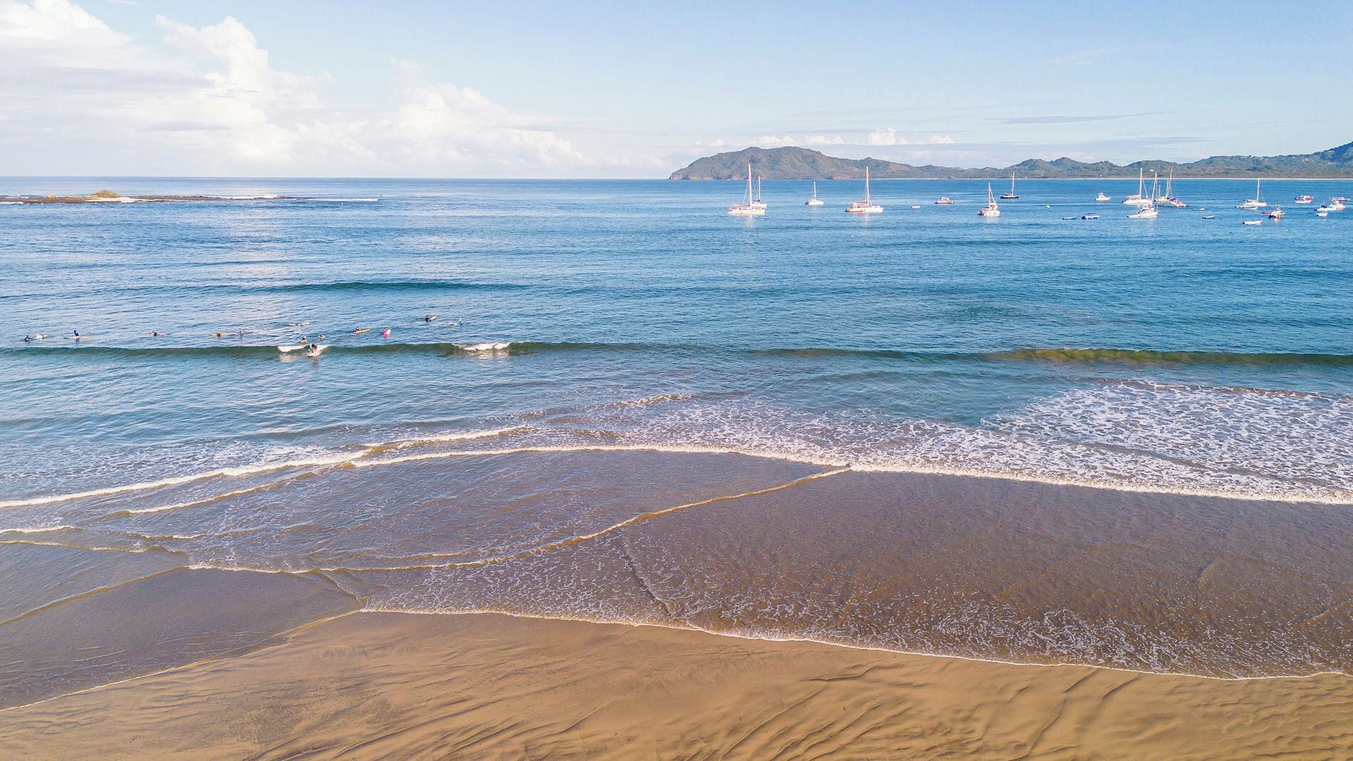Una spiaggia con onde, barche e colline sullo sfondo.