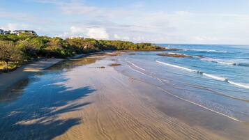 A beach with a sandy shore, waves, and a forested area with buildings in the background.