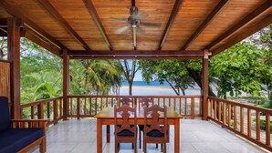 Una terraza de madera con una mesa y sillas, con vista a una playa.