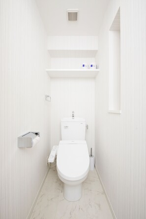 A small, white bathroom with a toilet, a shelf above the toilet, and a mirror on the right wall. - Residence Hotel Hakata 3 (Fukuoka)