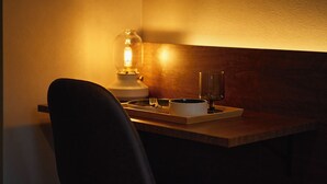 Un rincón tenuemente iluminado de una habitación con una mesa de madera, una silla, una lámpara y una bandeja con una taza y una copa.