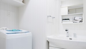 Un baño moderno con una decoración en blanco, lavadora integrada, un espejo grande y un tocador con lavabo y armarios.