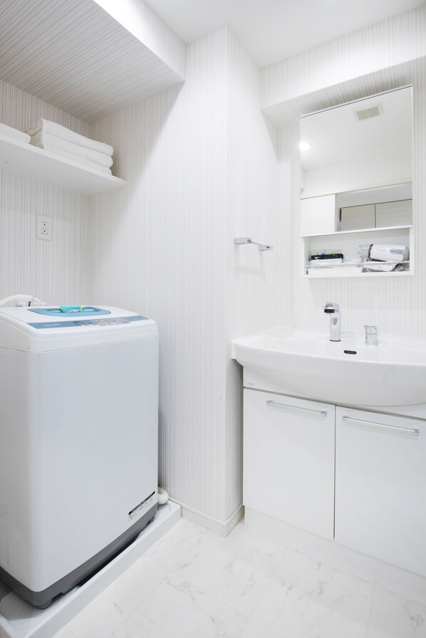 Un baño moderno con una decoración en blanco, lavadora integrada, un espejo grande y un tocador con lavabo y armarios.
