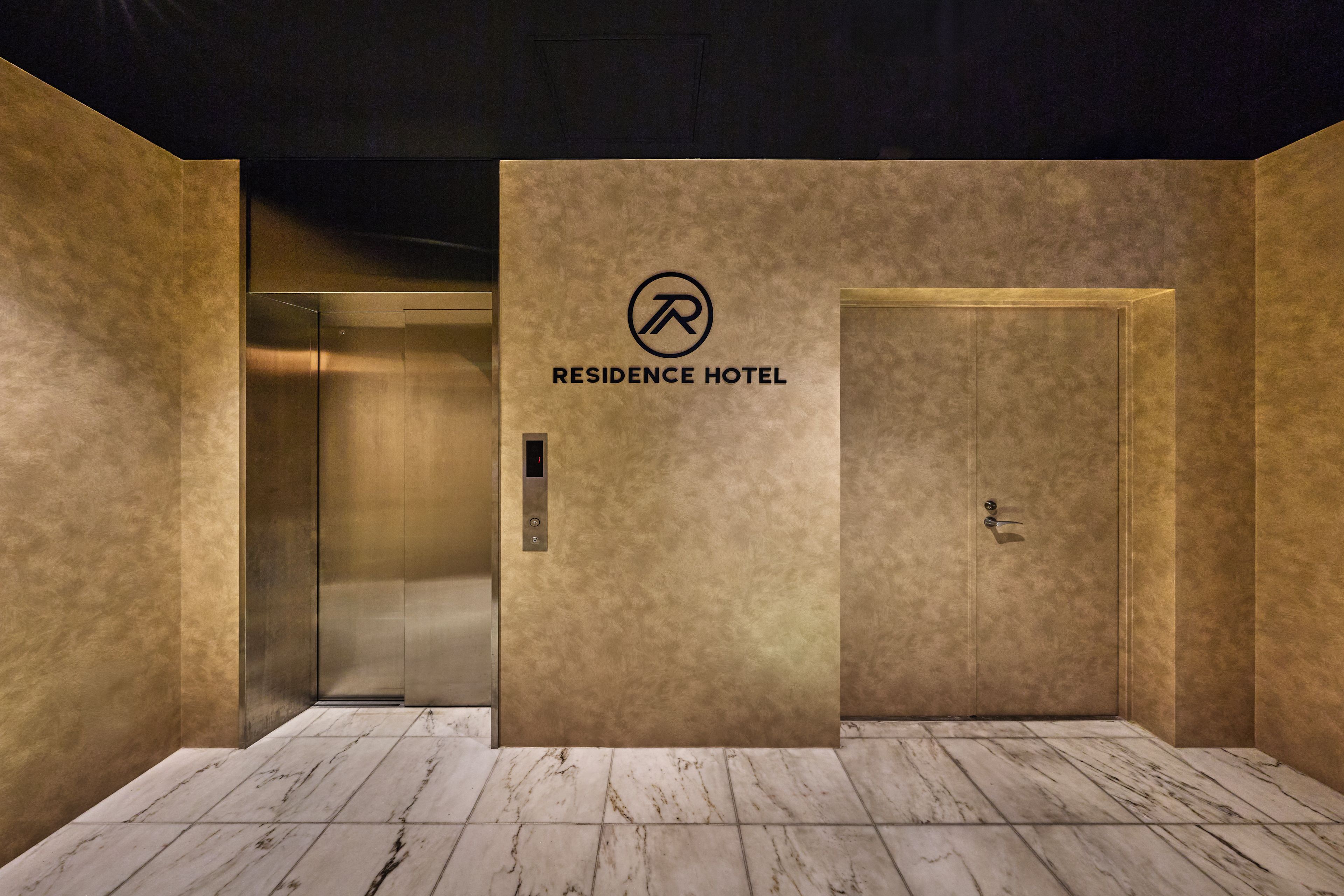 An elevator interior with a 'Residence Hotel' sign, a metallic elevator door, and a marble floor.