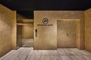 Een liftinterieur met een bordje 'Residence Hotel', een metalen liftdeur en een marmeren vloer.