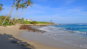 A beach with clear blue water, palm trees, and a building in the background. - Mirissa Beach Villa (Thalaramba)