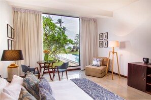 A hotel room with a large window, a bed, a desk with chairs, a sofa, and a lamp. - Mirissa Beach Villa (Thalaramba)