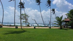 A grassy area with palm trees, a bench, and a view of the ocean. - Mirissa Beach Villa (Thalaramba)
