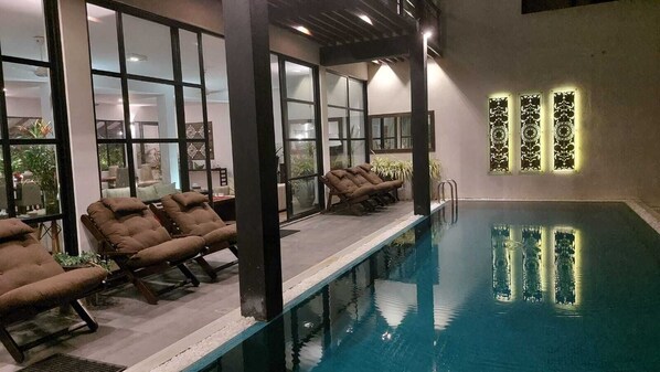 An indoor swimming pool with lounge chairs and a glass wall. - Mirissa Beach Villa (Thalaramba)