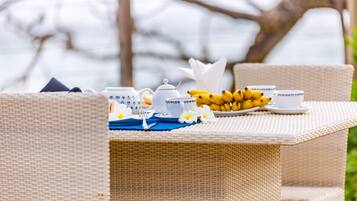 A wicker table set with tea cups, a teapot, a plate of bananas, and a blue placemat.