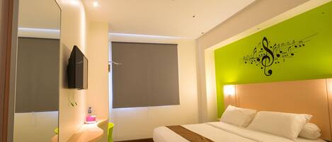 A modern hotel room with a bed, a TV, a desk with a chair, and a green accent wall.