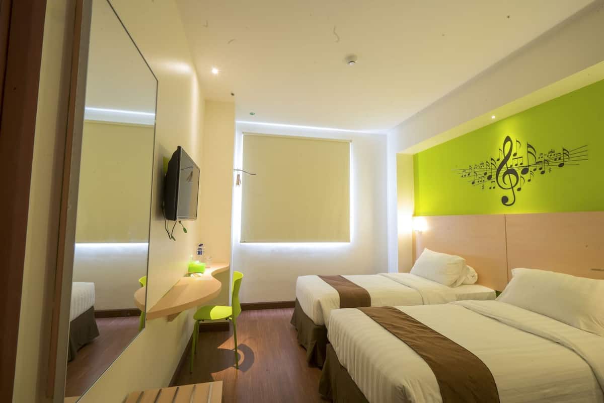 A hotel room with two beds, a mirror, a television, a window, and a green wall decoration.