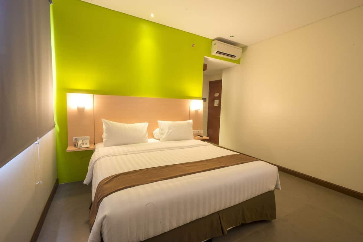A hotel room with a bed, bedside tables, an air conditioning unit, and a green accent wall.
