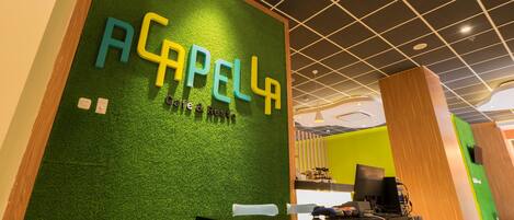 A reception area with a green wall and the name 'ACAPELLA' in large letters.