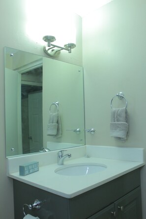 Une salle de bain avec un lavabo blanc, un grand miroir et deux serviettes suspendues à des porte-serviettes.