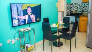 A kitchen with teal walls, a TV mounted on the wall, a dining table with chairs, and a refrigerator.