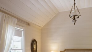 Een slaapkamer met een bed, nachtkastje, lamp, hanglamp, raam met gordijnen en een wandklok.
