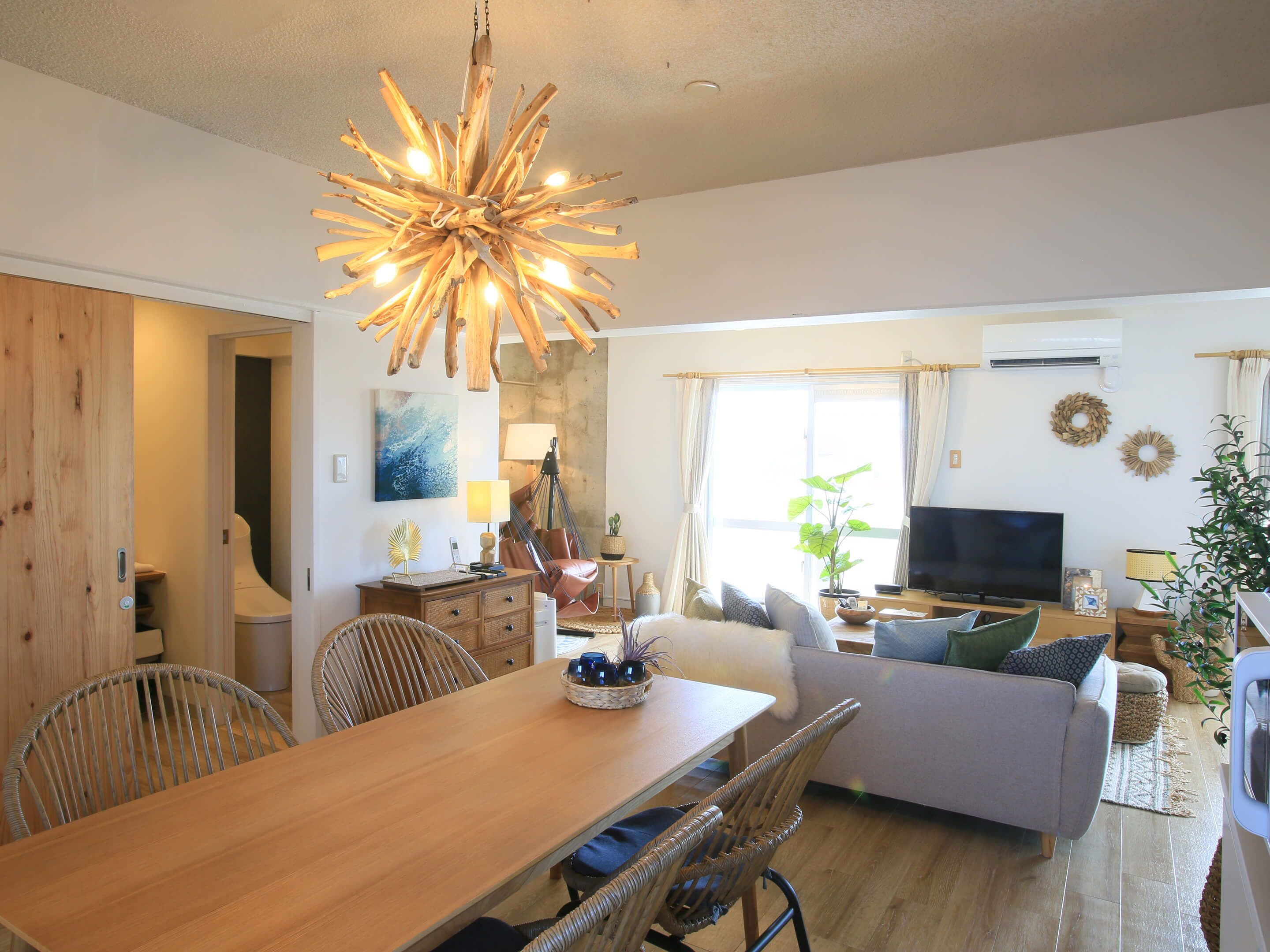 A modern living room with a wooden dining table, wicker chairs, a sofa, and a television.