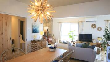 A modern living room with a wooden dining table, wicker chairs, a sofa, and a television.
