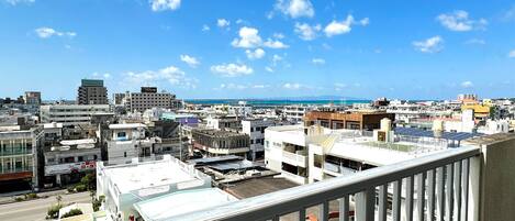 A cityscape with buildings, a clear sky, and a distant view of the sea.