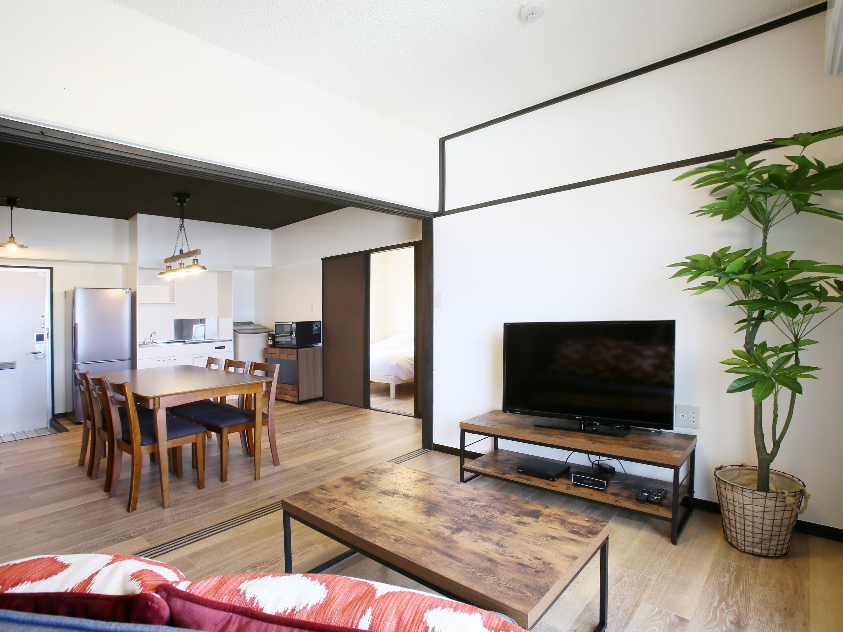 A compact living space with a dining area, kitchenette, and a TV on a wooden stand.