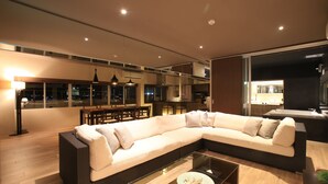 Un salon moderne avec un grand canapé d’angle, une table basse en verre et un coin repas comprenant une banquette et des chaises.