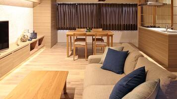 A modern living room with a wooden coffee table, a sofa with blue cushions, a dining area with a table and chairs, and a kitchen area with a stove.