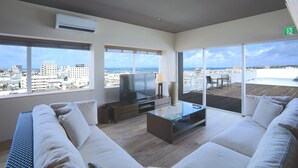 Un salon moderne doté d’un grand téléviseur, de sièges confortables et d’un balcon offrant une vue sur la ville.