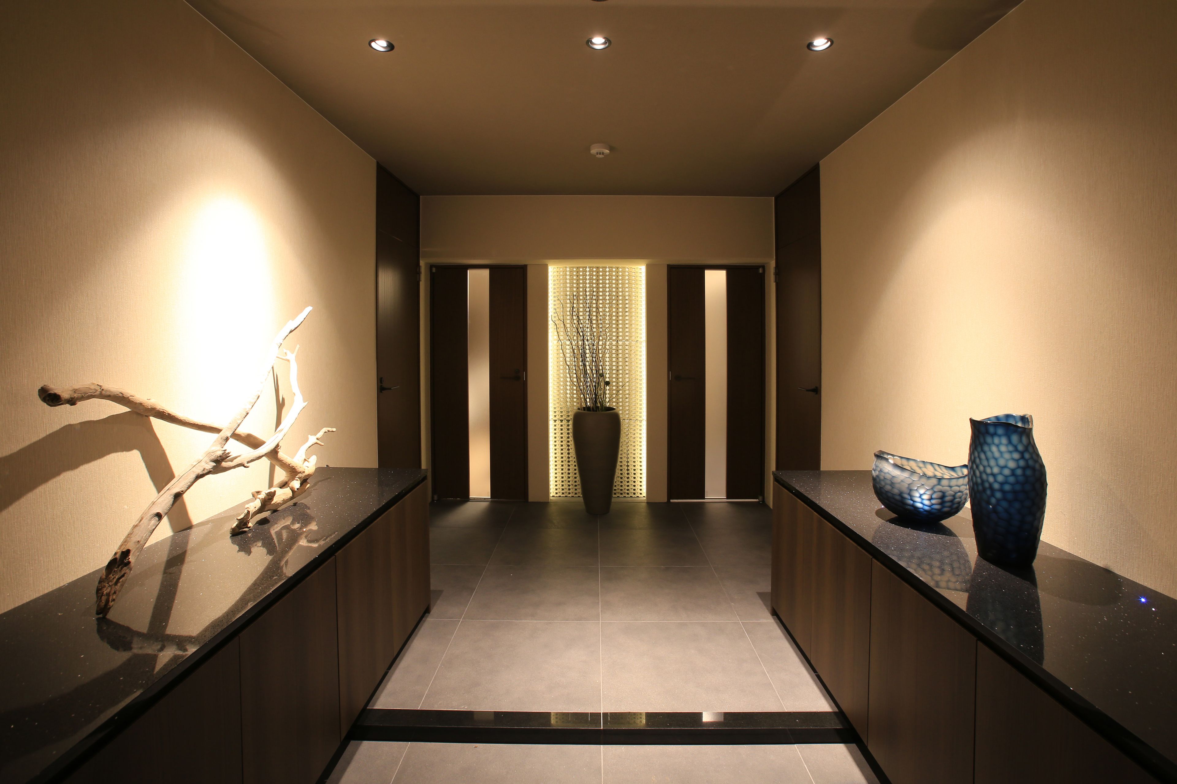A modern hallway with a reflective black floor, a wooden reception desk, and a decorative vase on the right.