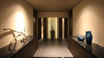 A modern hallway with a reflective black floor, a wooden reception desk, and a decorative vase on the right.