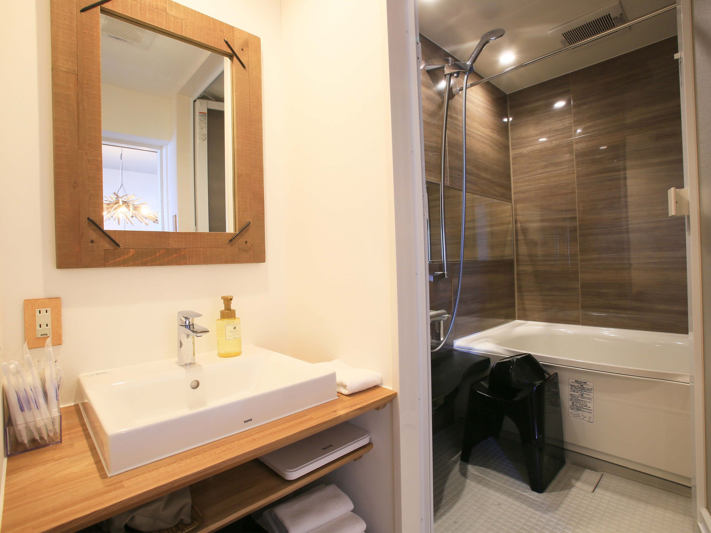Un baño moderno con tocador de madera, un espejo grande, un lavamanos blanco, un cabezal de ducha de mano y una bañera negra.