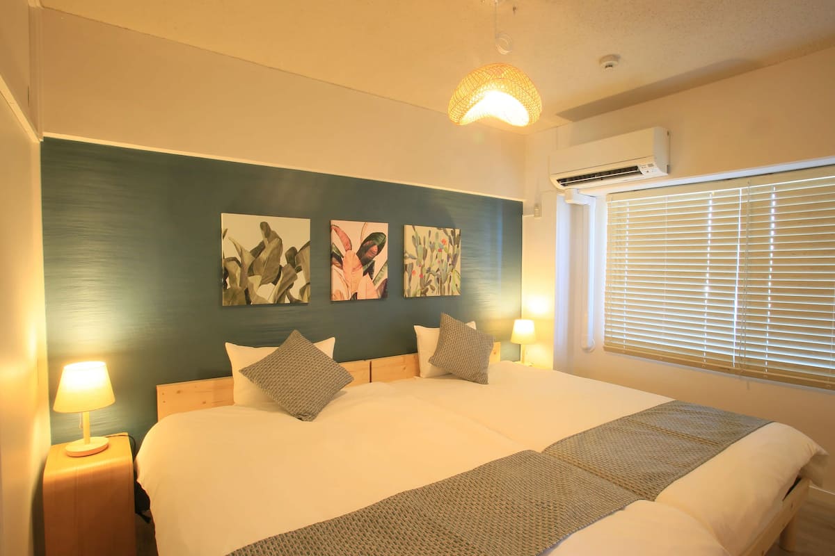 A bedroom with a large bed, two bedside tables with lamps, a ceiling light fixture, and three wall-mounted artworks.
