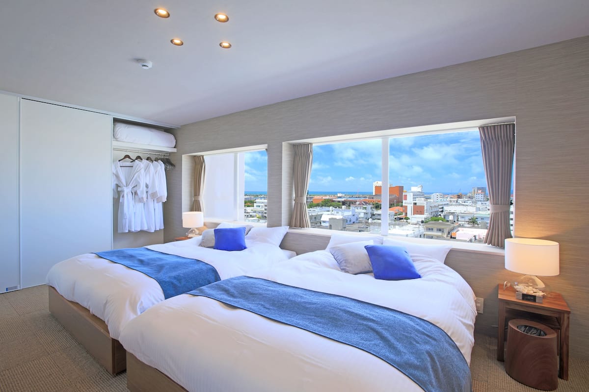 A hotel room with two beds, a view of the city, and a window with curtains.