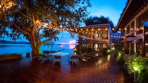 A wooden deck with lounge chairs and a table, overlooking a body of water at dusk. - Tamarina Bed & Beyond (Koh Samui)