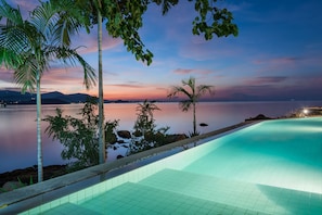 Una piscina con vista a un lago tranquilo y montañas al atardecer.