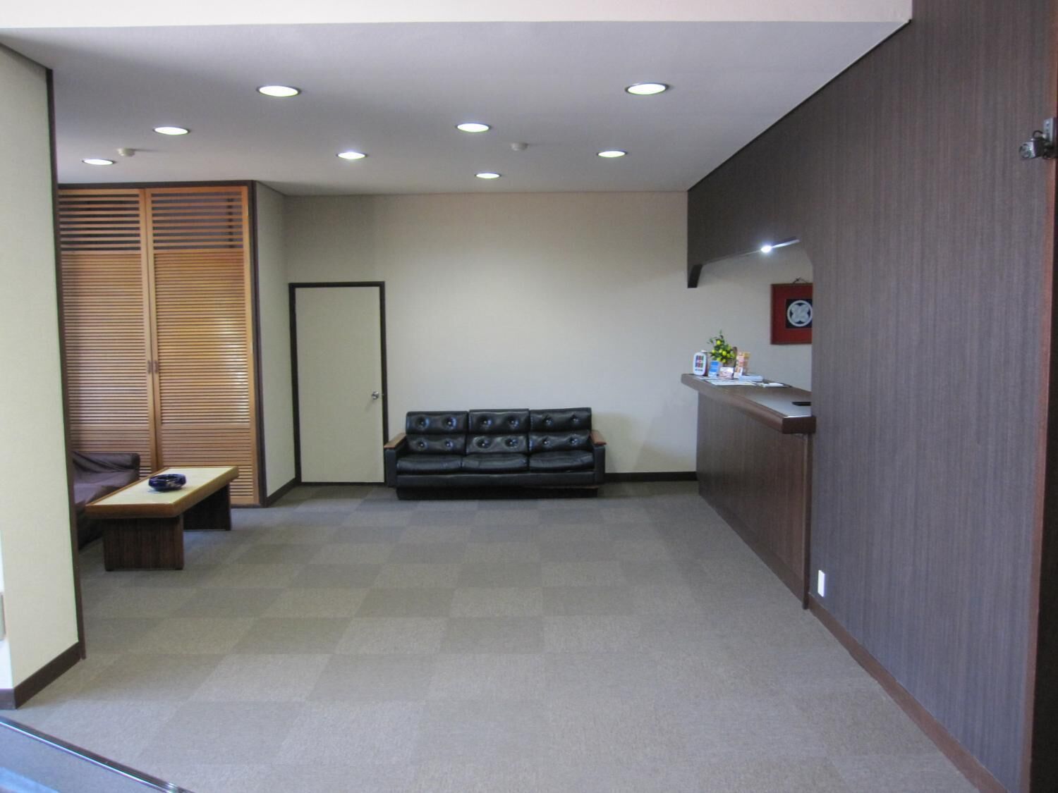 A reception area with a sofa, a small table, a wooden cabinet, and a reception desk.
