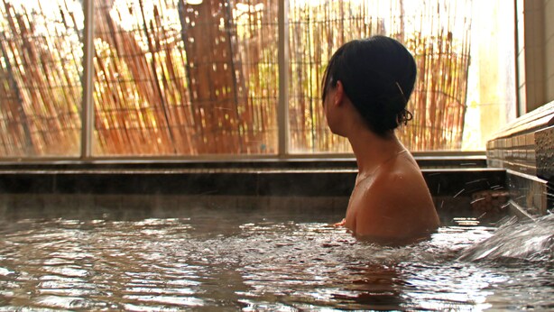 A person in a hot tub with a view of bamboo outside the window. - Masuya Ryokan (Izumo)