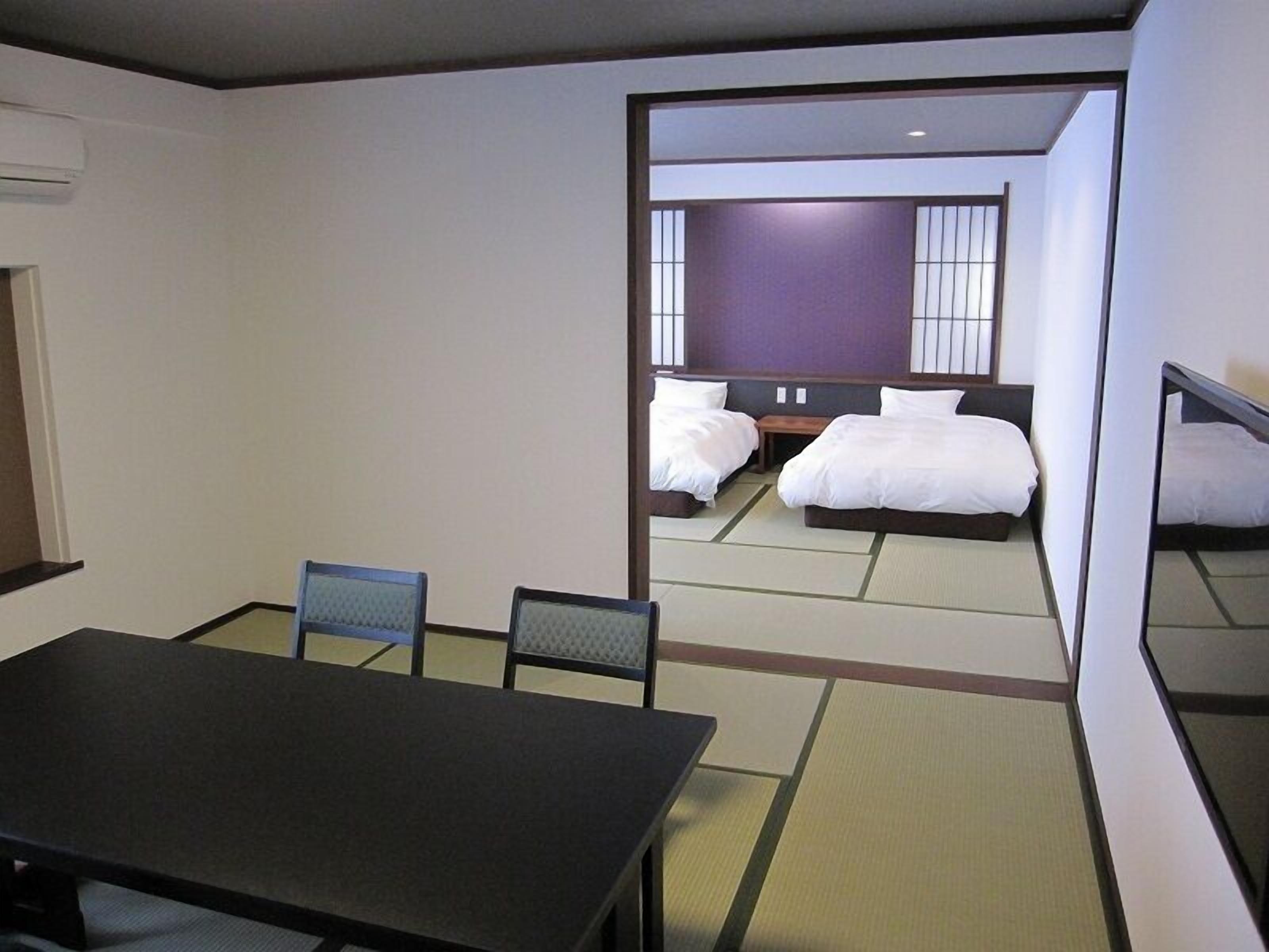 A hotel room with a large bed, a smaller bed, a table, and two chairs.