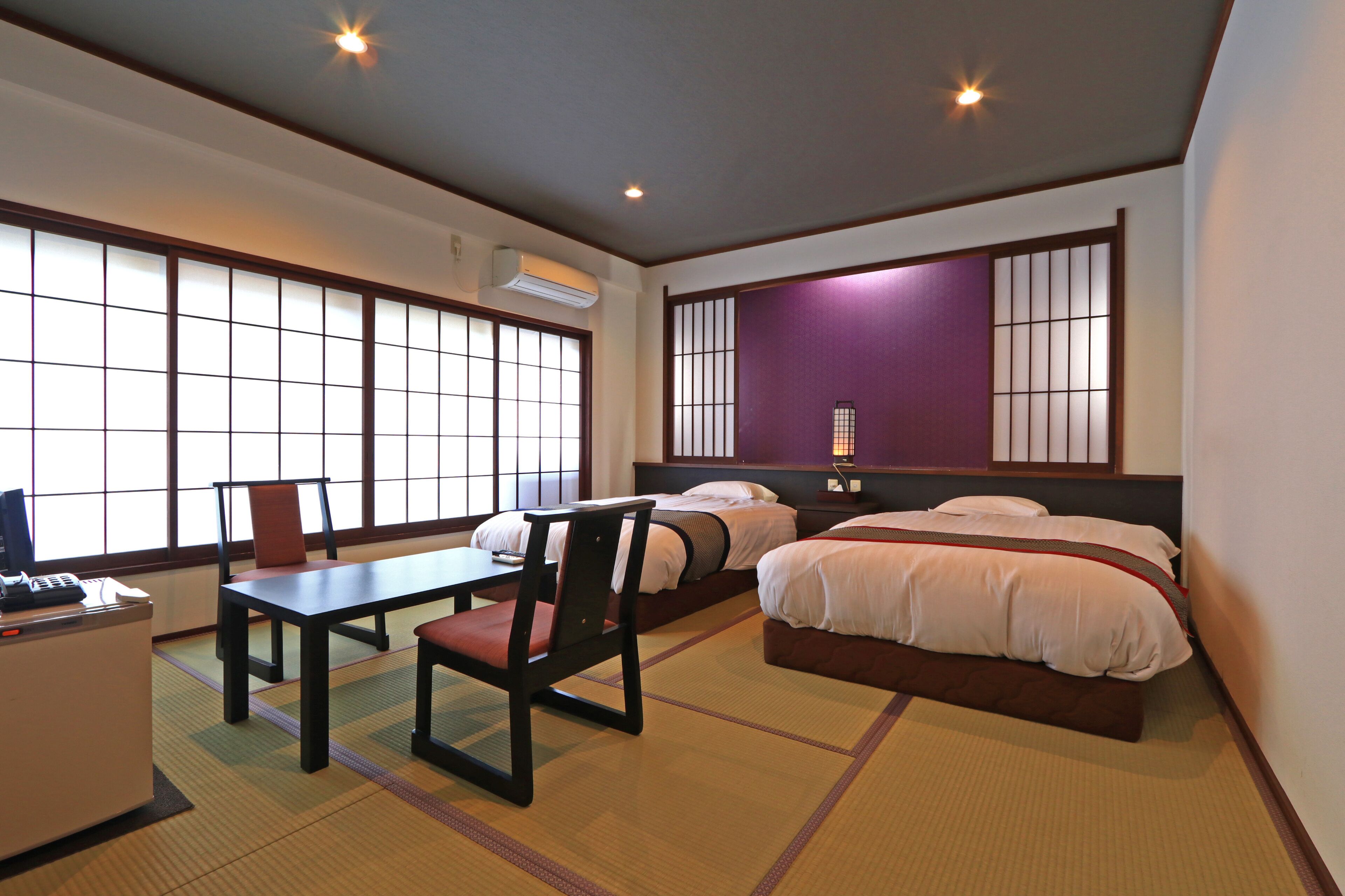 A hotel room with tatami mats, a desk with a chair, two beds, and a large window with a view.