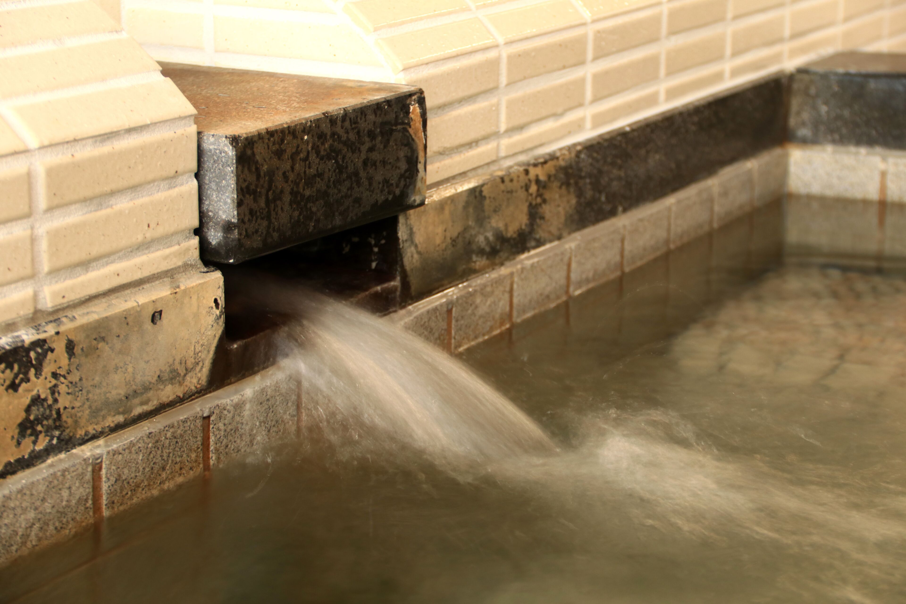A close-up of a water feature with flowing water, a tiled wall, and a dark-colored ledge.