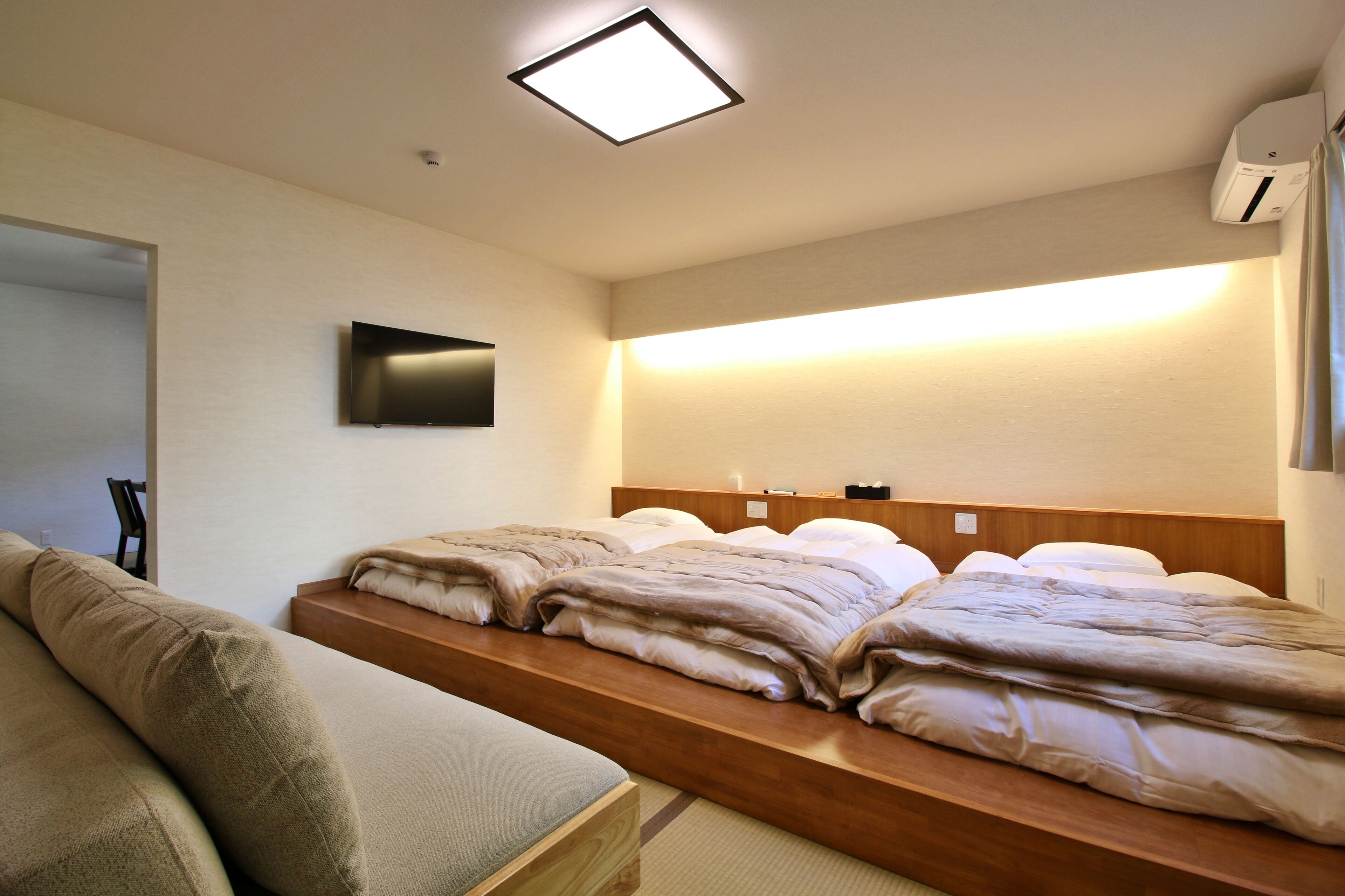 A hotel room with a wooden bed frame, a flat-screen TV mounted on the wall, and a bedside table with a lamp.