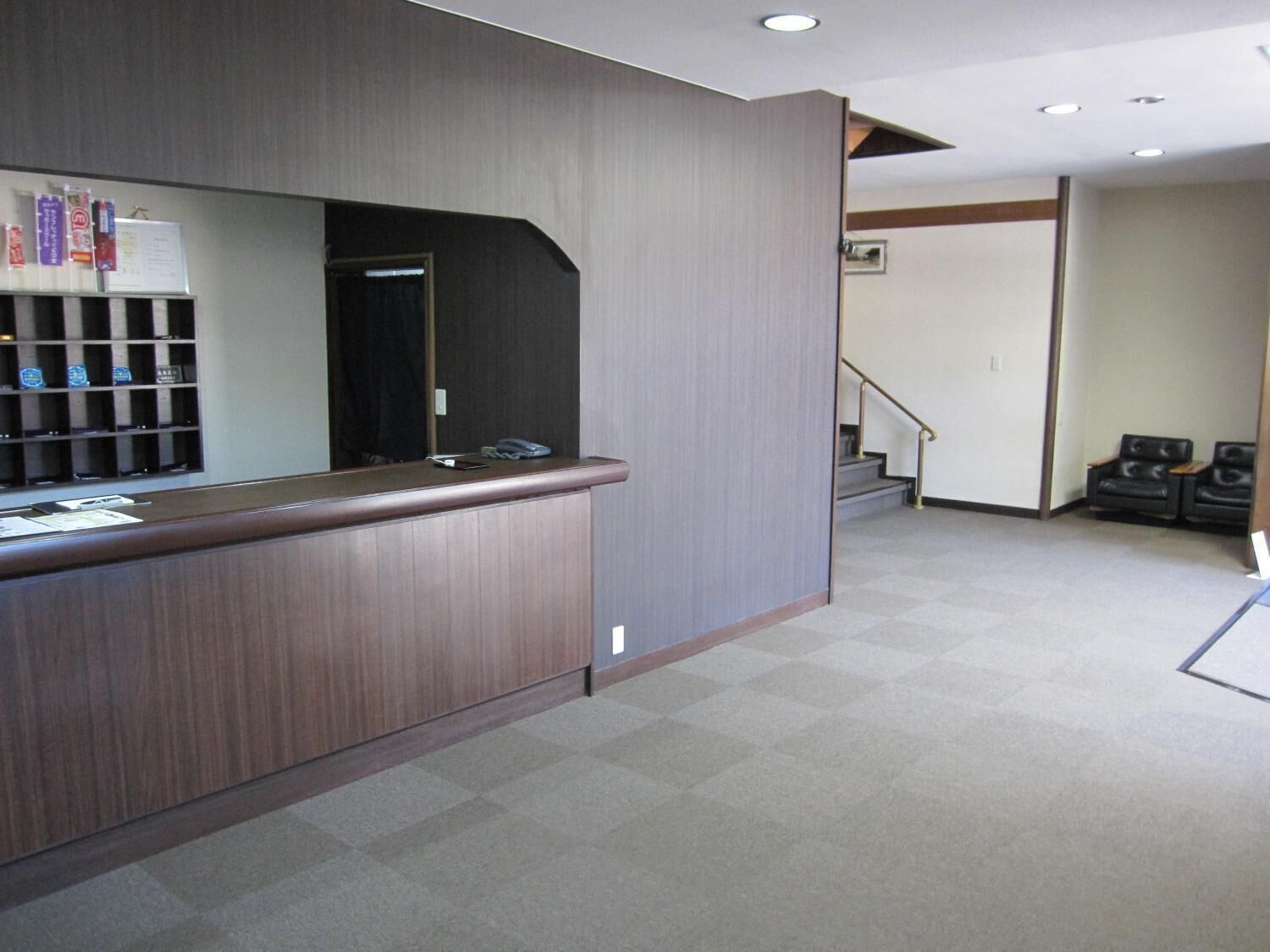 A reception area with a wooden counter, a bulletin board, and a staircase leading to another floor.
