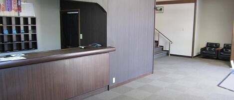 A reception area with a wooden counter, a bulletin board, and a staircase leading to another floor.