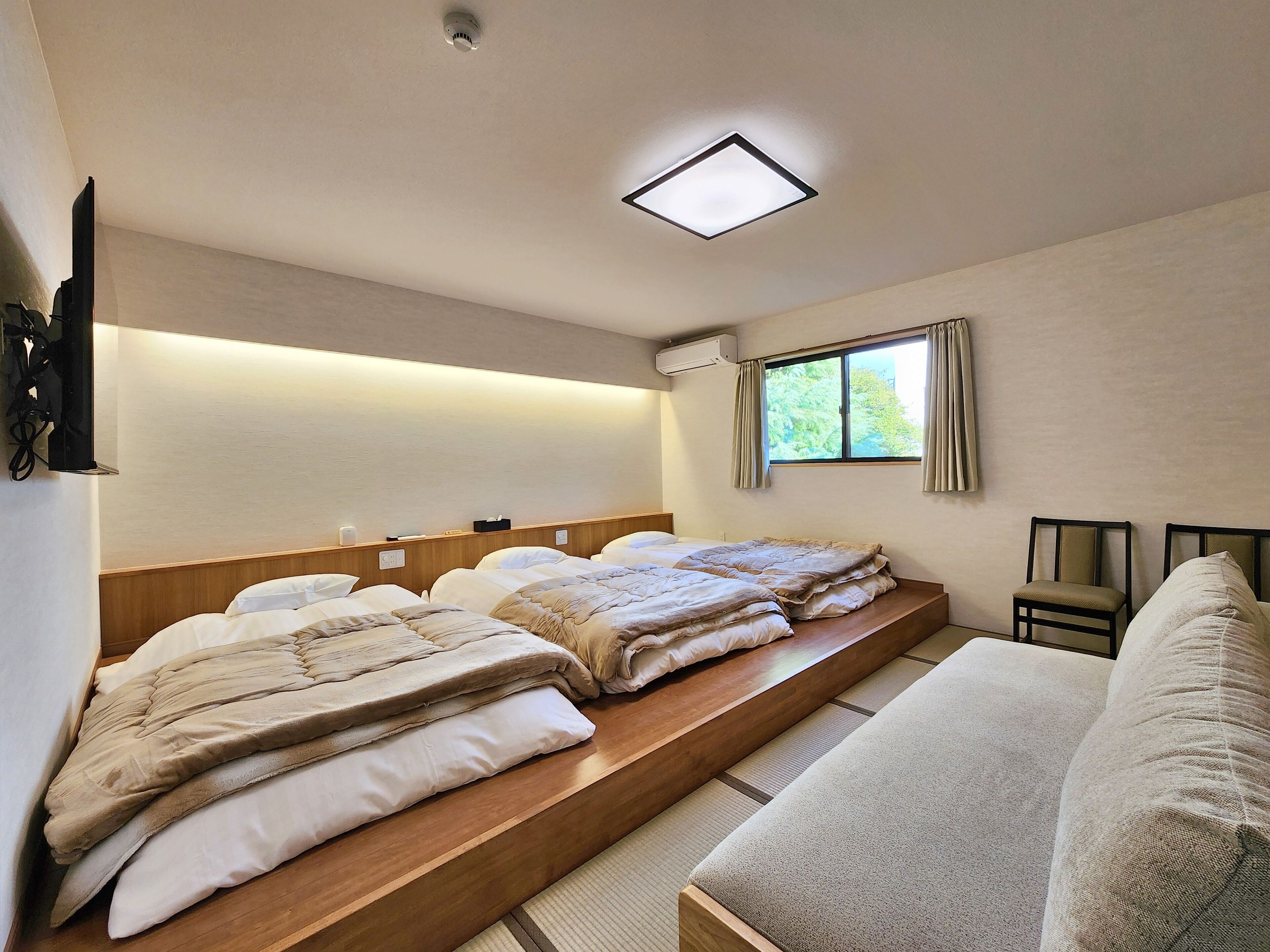 A hotel room with a bed, a sofa, a flat-screen TV, a window with curtains, and a ceiling light.
